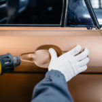 man flattening vinyl film on a car using a heat gun