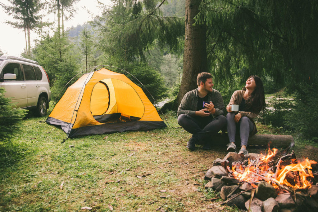 couple in front of bonfire with tent and car