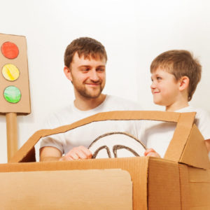 father son driving cardboard car at home scaled e1586832654122