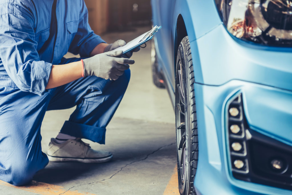 mechanic holding a clipboard while checking a car