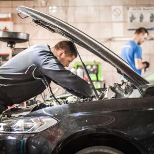 mechanic performs under the hood inspection of a car