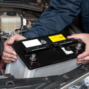 mechanic loads car battery into engine bay