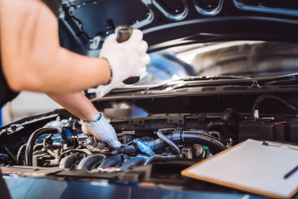 mechanic checking car engine using a flashlight