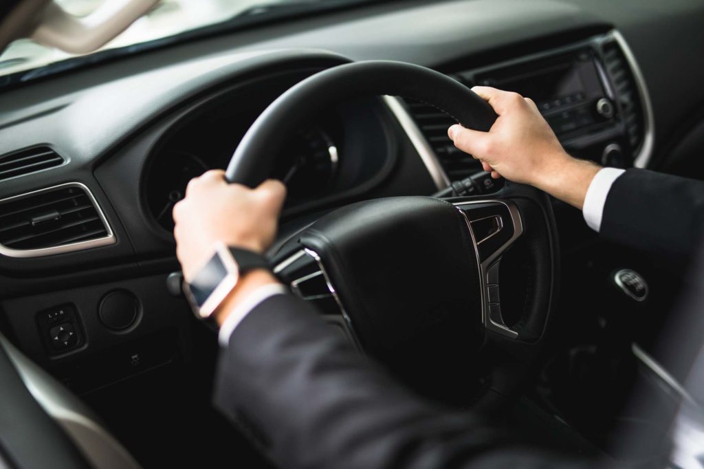 male driver hands on car steering wheel focused