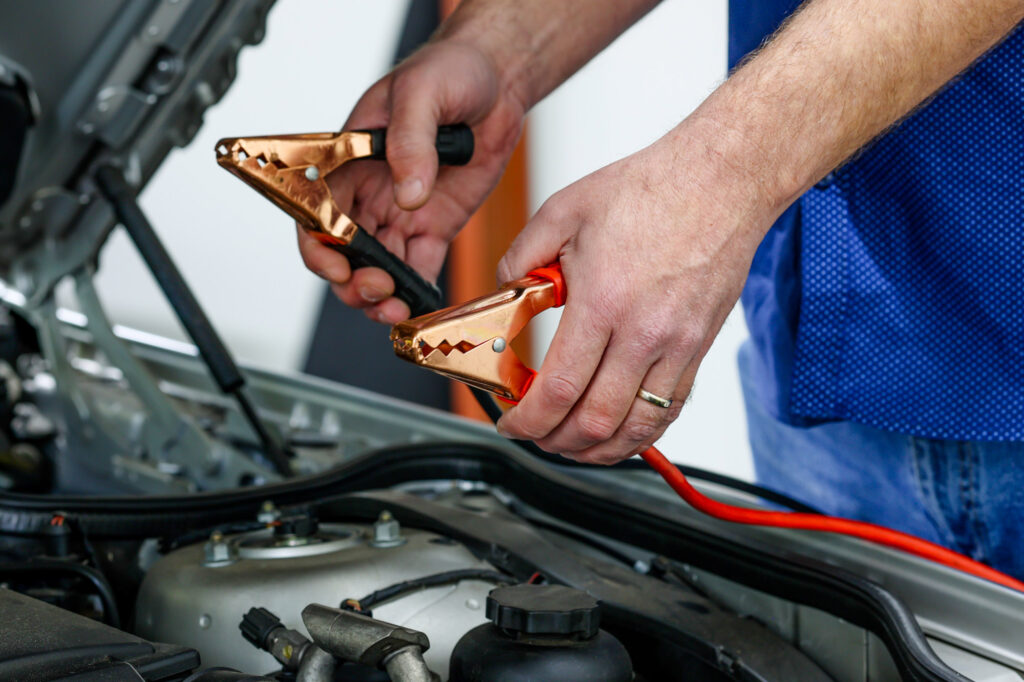 hand holding jump start car cables to recharge car battery