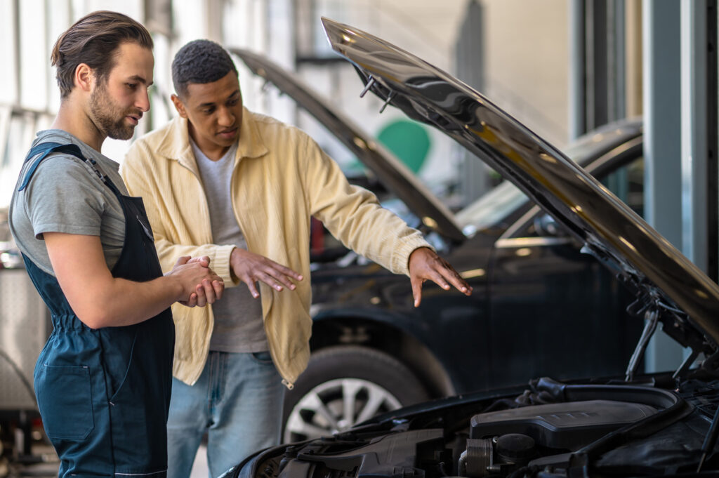 Mechanic,Looking,Into,Hood,And,Customer,Telling,Problem