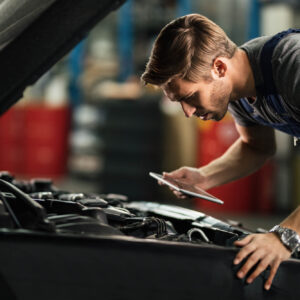 Young,Auto,Mechanic,With,Touchpad,Examining,Car,Engine,In,Repair