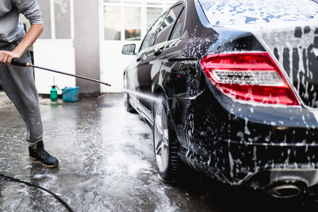 man using high pressure water to clean car