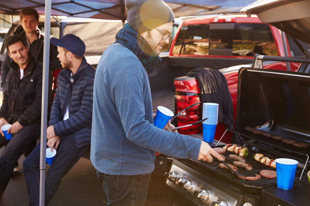 man enjoying summer cookout next to cars