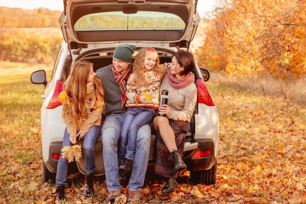 family sitting on a car trunk during fall