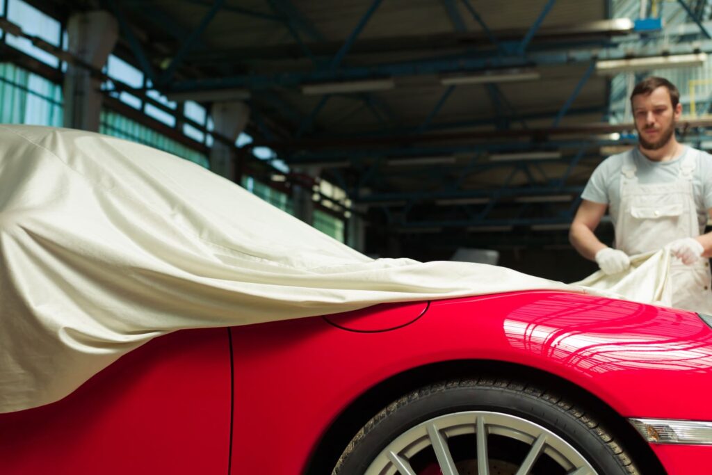 man removing car cover of a red vehicle